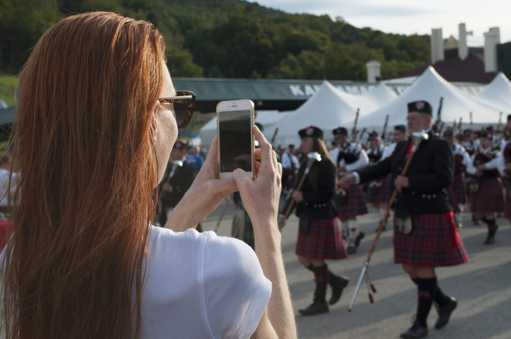 fashion blogger taking picture of scottish bagpipers marching in unison at highland games